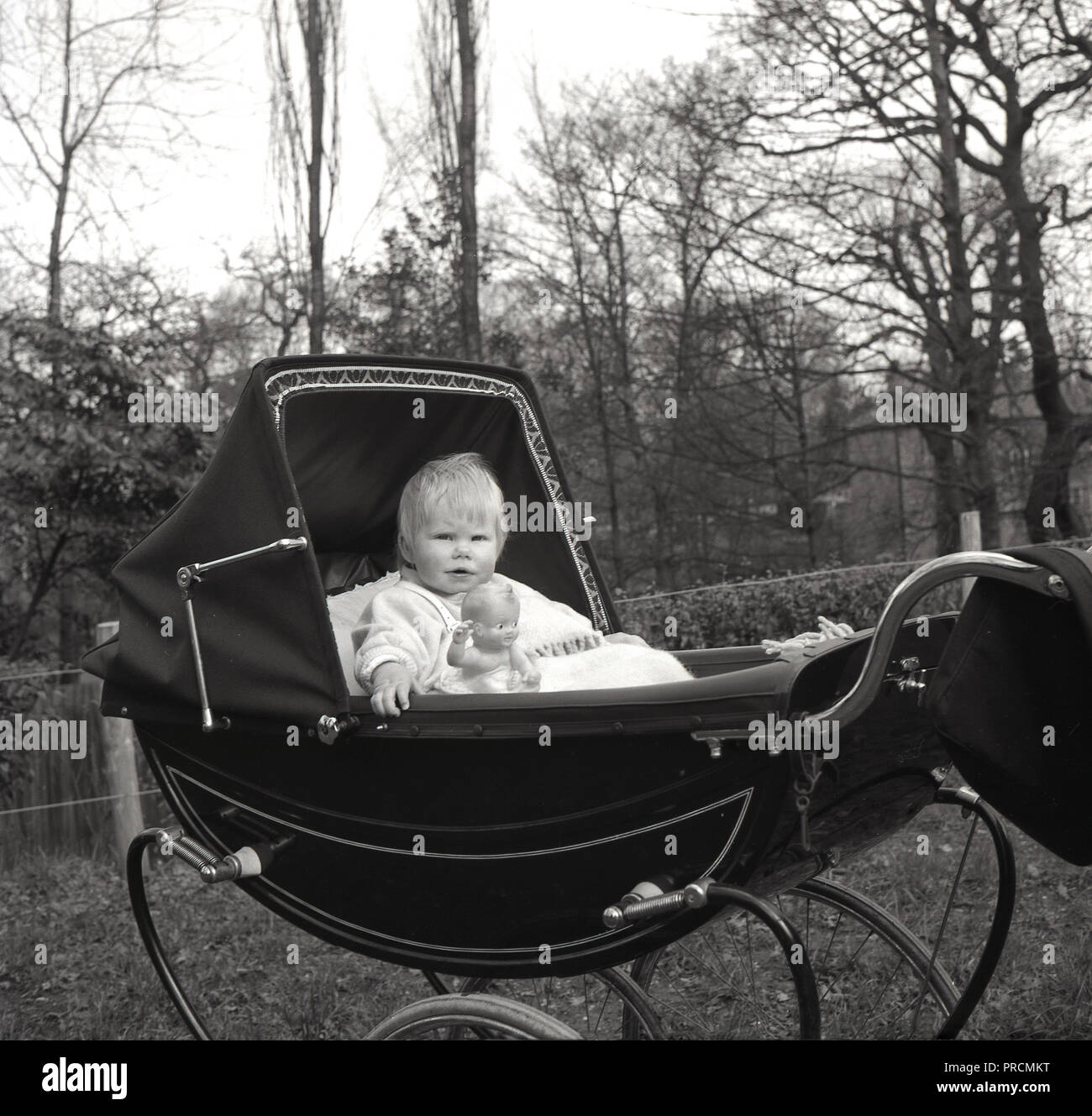 1950, historische, Kind, ein Junge (Kleinkind) aufrecht sitzend in einem  traditionellen Alkoven baby Schlitten oder Kinderwagen mit Kapuze, mit  seinem Spielzeug Abbildung neben ihm, England, UK Stockfotografie - Alamy