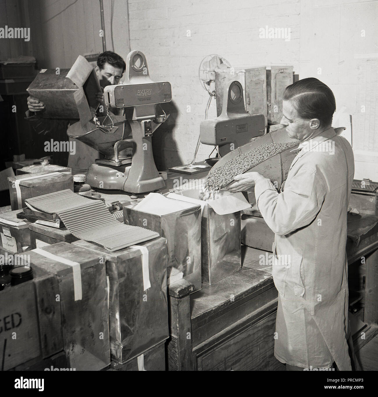 1950er historischen, männliche Arbeitnehmer wiegen und Medikamente - Tabletten und Pillen - in Boxen in der pharmazeutischen Gesellschaft von Arthur Cox, Brighton, England, UK. Im Jahr 1839 begann, Cox von Brighton wurde zu einem führenden britischen Hersteller und weltweiter Lieferant von medizinischen Produkten und Medikamenten in Tabletten-, Creme- und flüssiger Form. Stockfoto