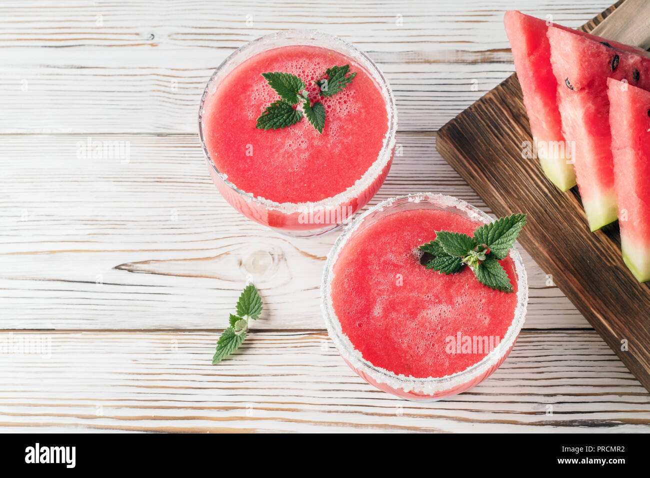 Trinken Smoothies aus roten Wassermelone in Glas Geschirr eingerichtet Weißzucker und Minze Stück Obst auf Schneidebrett weißer Tisch Konzept von heilen Stockfoto