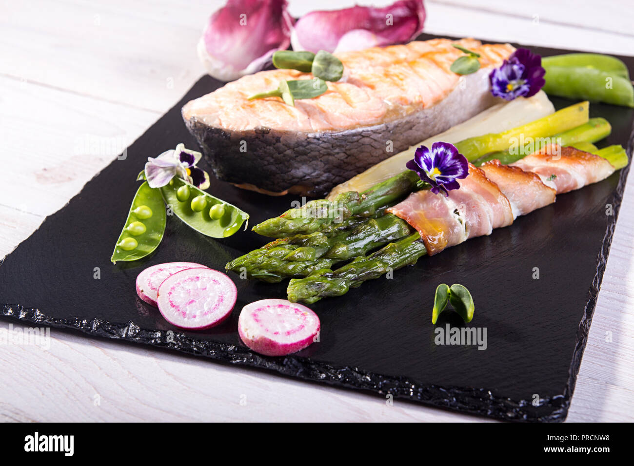 Gegrillter Lachs im Ofen gebacken, mit grünem Spargel im Speckmantel auf  schwarzem Hintergrund gewickelt. Overhead Stockfotografie - Alamy