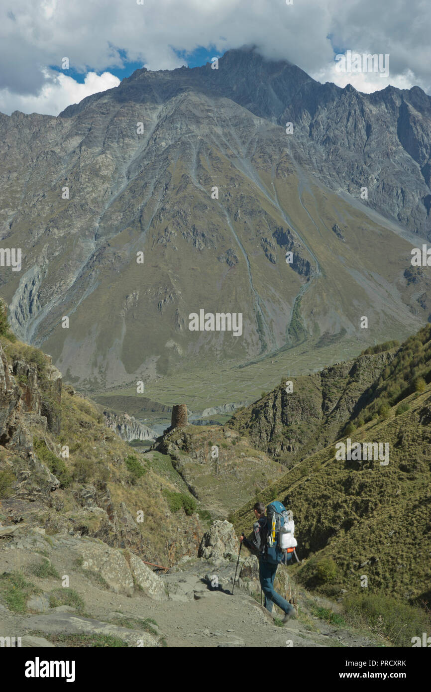 Touristen Trekking in der Nähe der Kirche der Heiligen Dreifaltigkeit Gergeti durch den Fluss Chkheri, unter dem Berg Kazbegi liegt auf einer Höhe von 2170 Metern in den Kaukasus, Georg Stockfoto