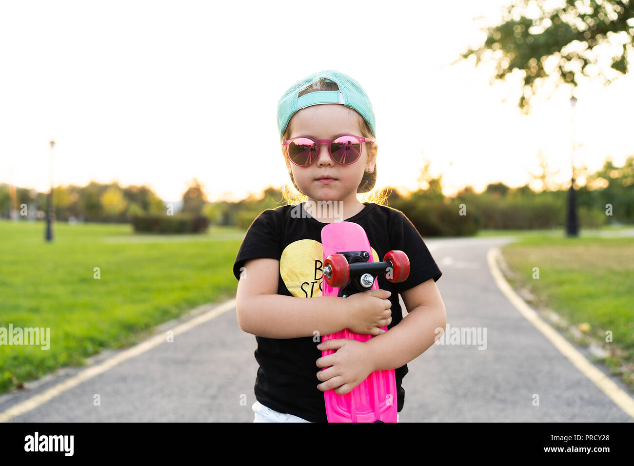 Mode Mädchen Kind mit Skateboard das Tragen einer Sonnenbrille und hipster Shirt. Stockfoto