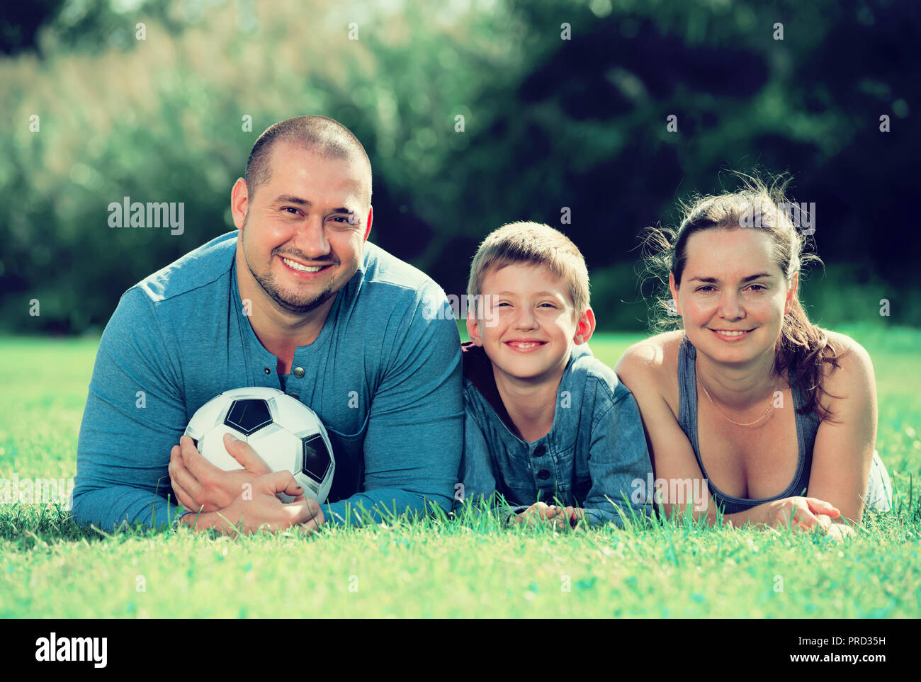 Mutter, Vater und Teenager Sohn im Gras mit Fußball liegen Stockfoto