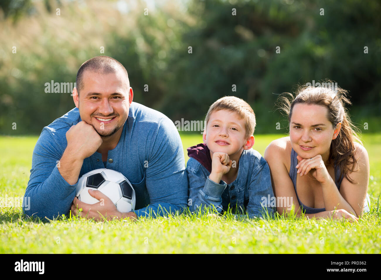 Fröhliche Teenager, Mutter, Vater und Sohn in das Gras mit Fußball liegen Stockfoto