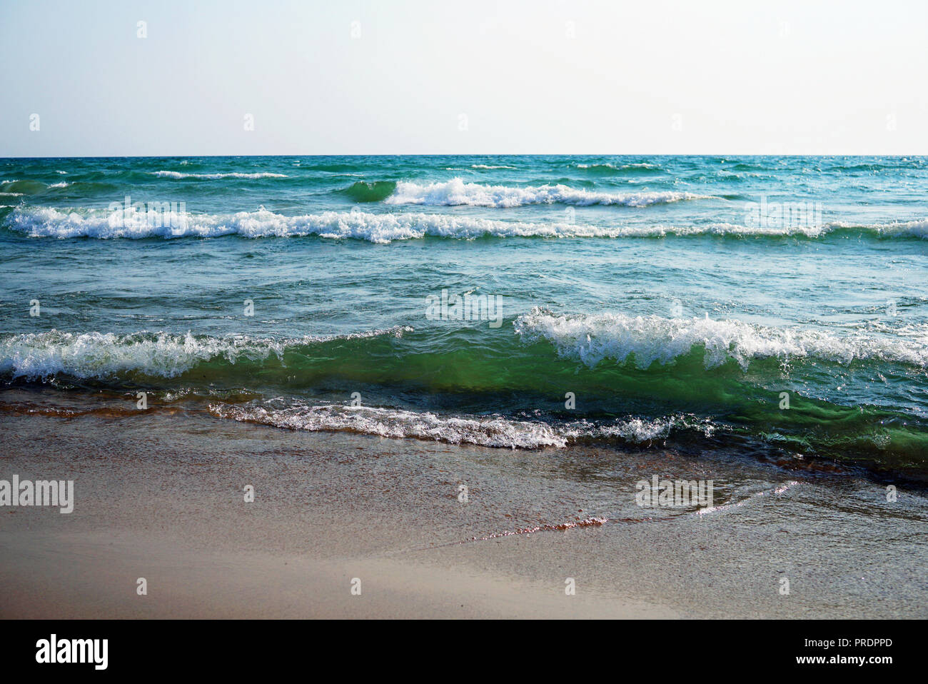 Tosende Meer auf einem sonnigen windigen Tag. Große Wellen mit weißen Schaum auf dem Kamm steigen über die Oberfläche des Wassers und zum Ufer laufen. Schönes helles g Stockfoto