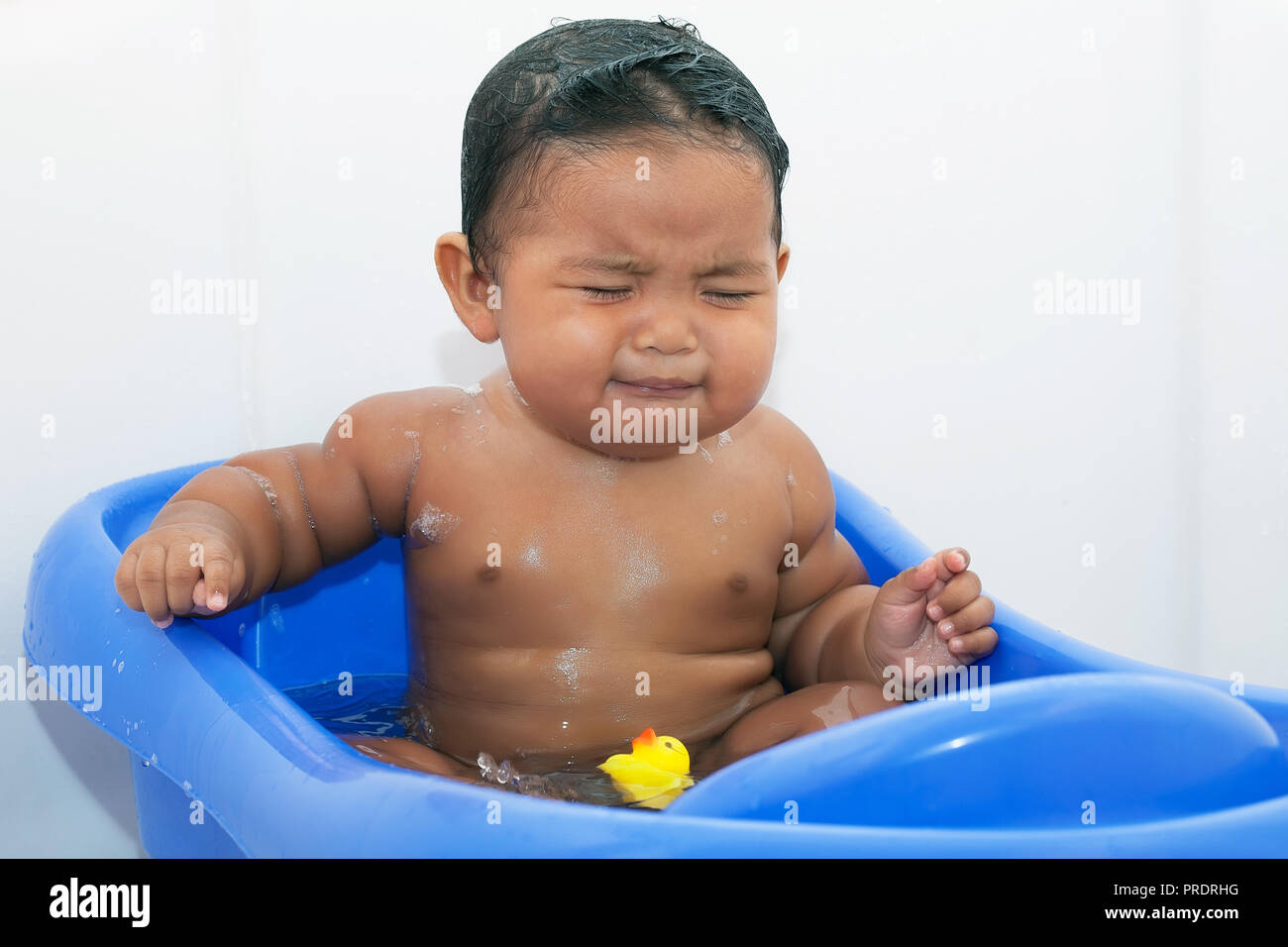 Chubby Baby in der Badewanne in eine Babywanne, sitzen im Wasser mit Seife und Weinen suchen umgekippt Stockfoto