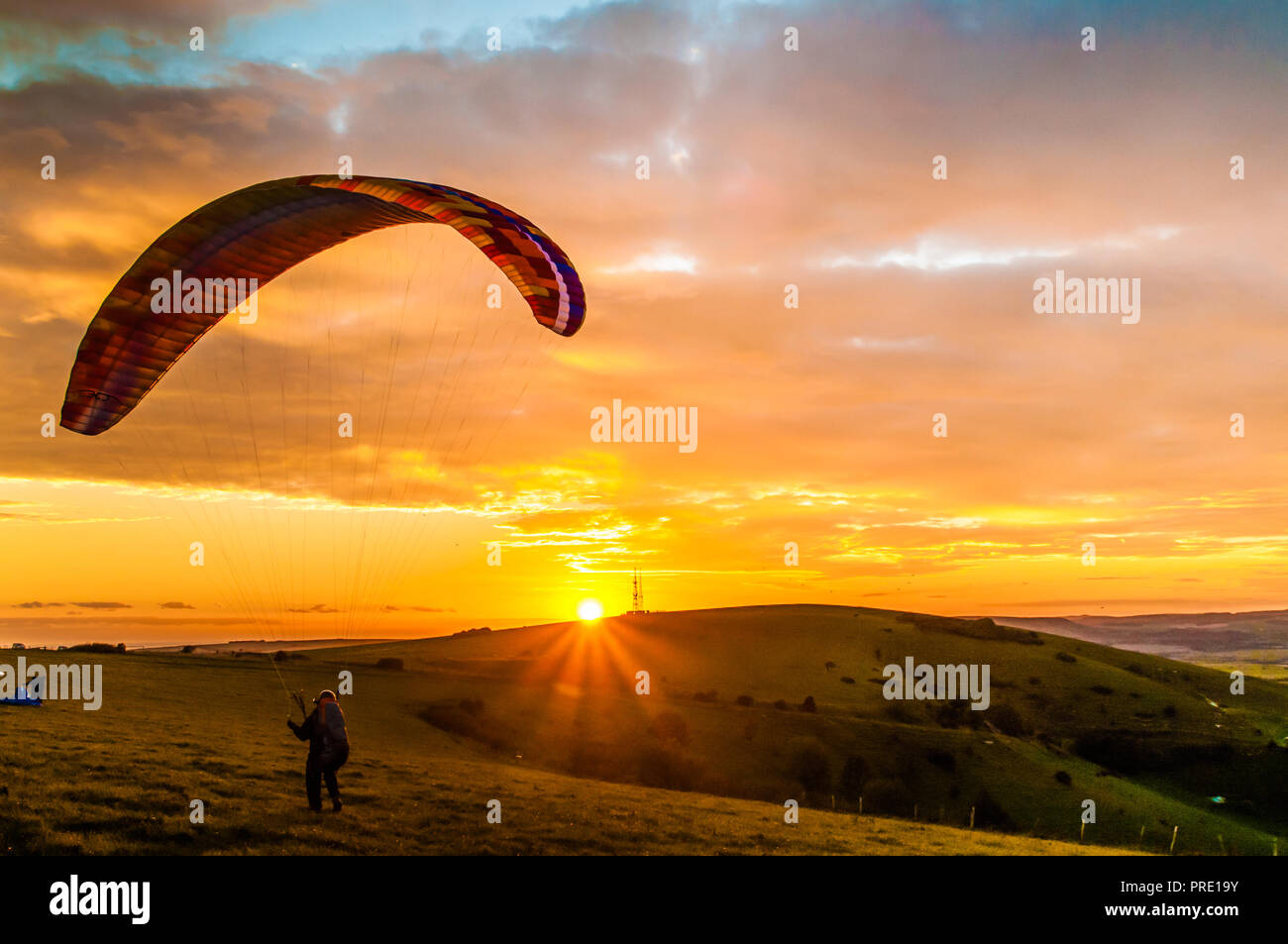 Firle Beacon, Lewes, East Sussex, Großbritannien. Oktober 2018..Gleitschirmflieger shouettierten gegen den Sonneneingang unter der Wolkendecke von Altocumulus. Das Fliegen am Standort in den South Downs war nur für kurze Zeit um den Sonnenuntergang möglich, da sich der starke wehende Wind aus dem Nordwesten zu sicheren Flugbedingungen beruhigte. Stockfoto