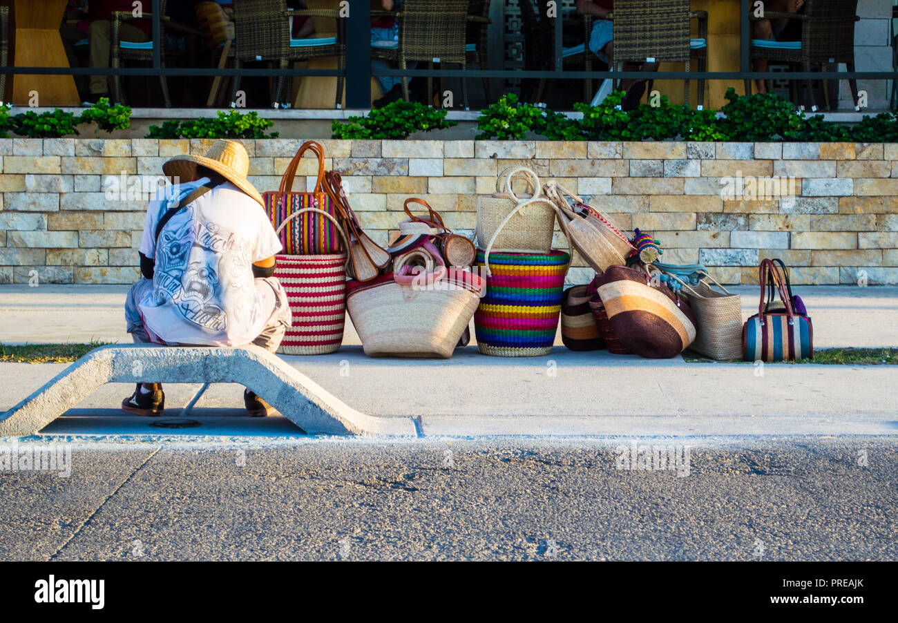 Mexikanischer Straßenhändler, der Taschen verkauft und vor einem teuren Restaurant wartet. Beispiel für wirtschaftliche Ungleichheit. Stockfoto