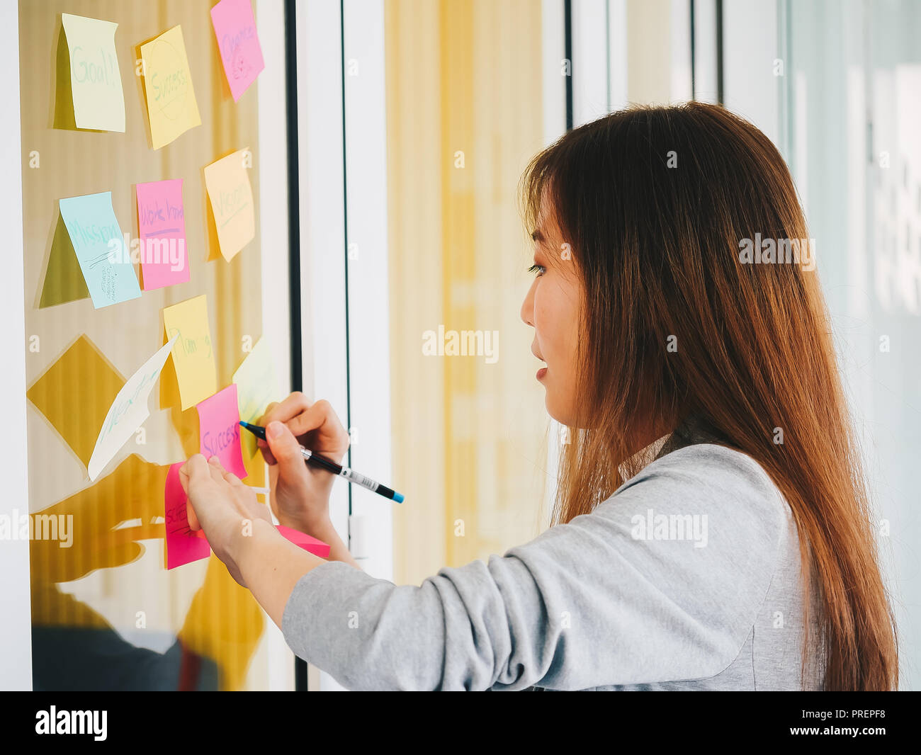 Nachdenklich Geschäftsfrau auf Haftnotizen Suche stecken und denken Brainstorming auf Glas Wand in kreative Büro Stockfoto