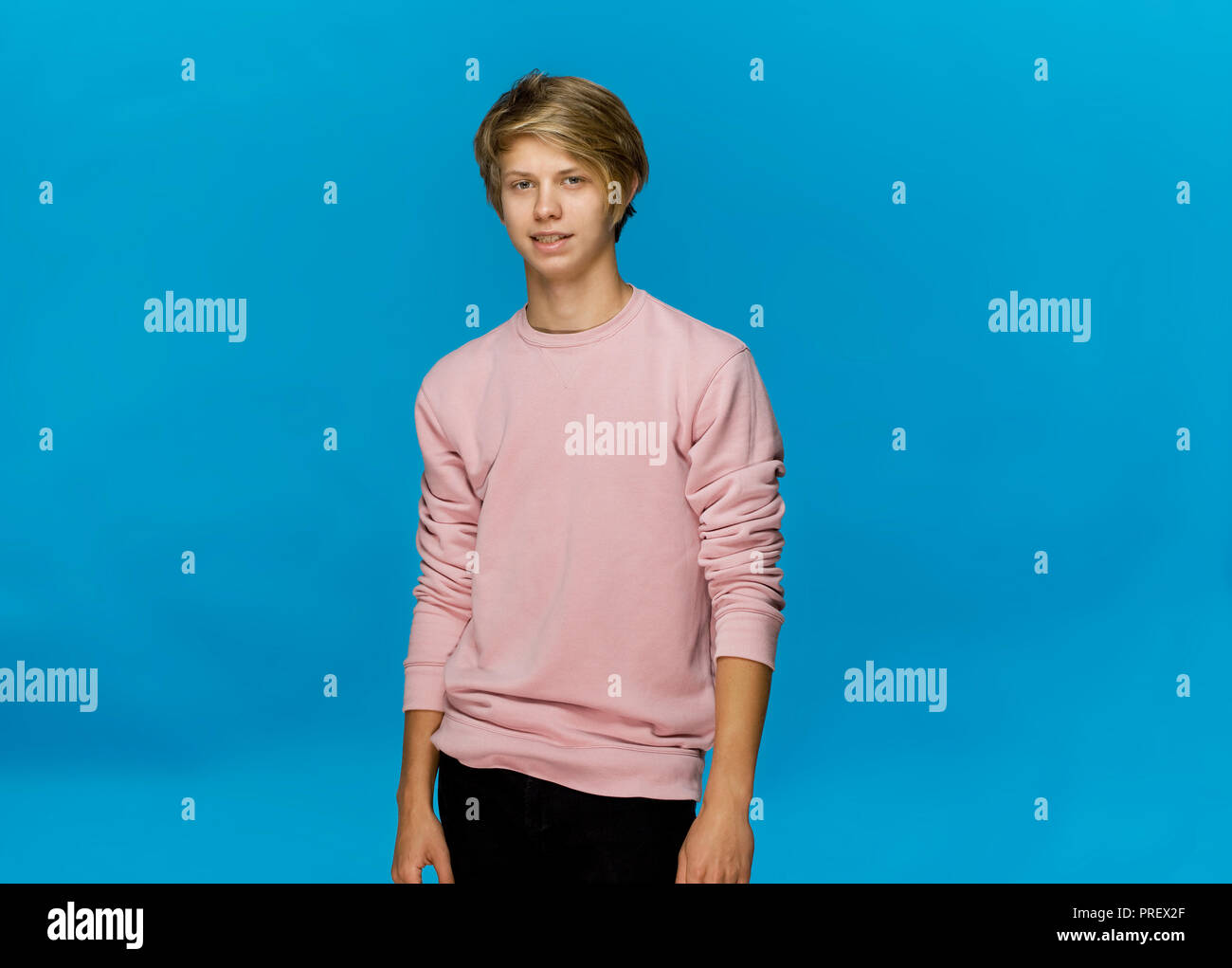 Stattliche glücklich lächelnde junge Mann mit rosa Bluse studio Portrait gegen blaue Wand Stockfoto
