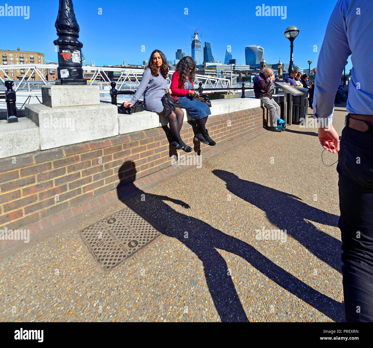 Leute sitzen auf der Mauer auf der South Bank, London, England, UK. Mittag. Stadt London Skyline hinter Stockfoto