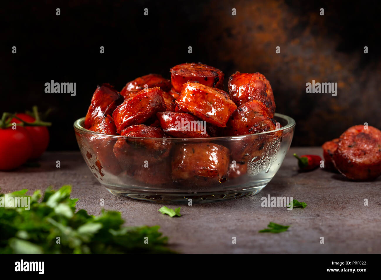 Scheiben von gebratenen Würstchen in einem transparenten Schüssel mit grüner Petersilie und Kirschtomaten Stockfoto