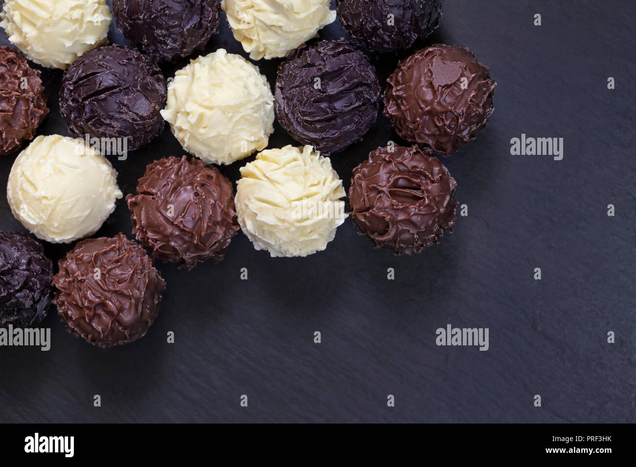 Leckere Schokolade Trüffel auf schwarzem Stein. Sortiment an feinen Pralinen in weißer dunkler und Milchschokolade. Stockfoto