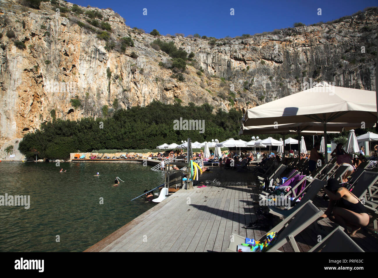 Vouliagmeni Athen Griechenland Touristen, die am Vouliagmeni-See ein Naturbad sonnen - war einst eine Höhle, aber das Höhlendach fiel durch Erosion von t ein Stockfoto