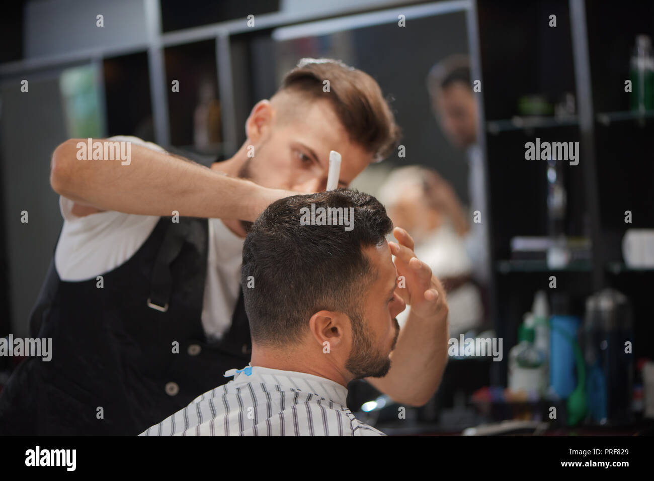 Zuversichtlich männlich Friseur styling Bart des Mannes und stilvolle Haarschnitt. Client Bärtigen warten, während Friseur Pflege sein Haar. Konzept der Barbershop, Beauty und Haare. Stockfoto