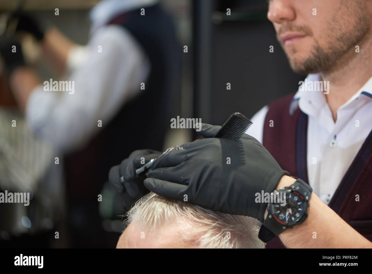 Nicht erkennbare Gesichter der Friseur- und seinem Klienten im barbershop. Männliche Friseur mit schwarzen Handschuhe beim Arbeiten mit Haar. Friseur schneiden das graue Haar des Menschen mit Schere und Kamm. Stockfoto
