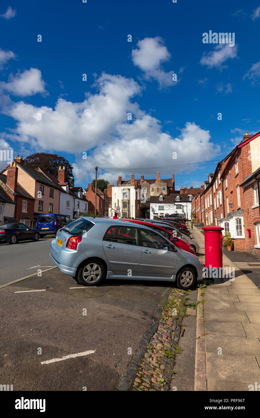 Autos geparkt auf untere Breite Straße Ludlow, der Blick auf die historischen Häuser und Tor den Hügel hinauf in Richtung Stadtzentrum, Shropshire, Großbritannien Ruine Stockfoto