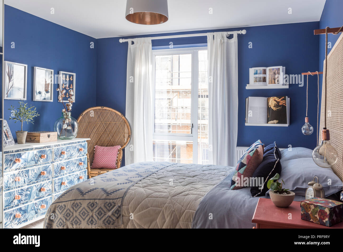 Korbstuhl und Blatt gemusterten Kommode im blauen Schlafzimmer von London Stockfoto