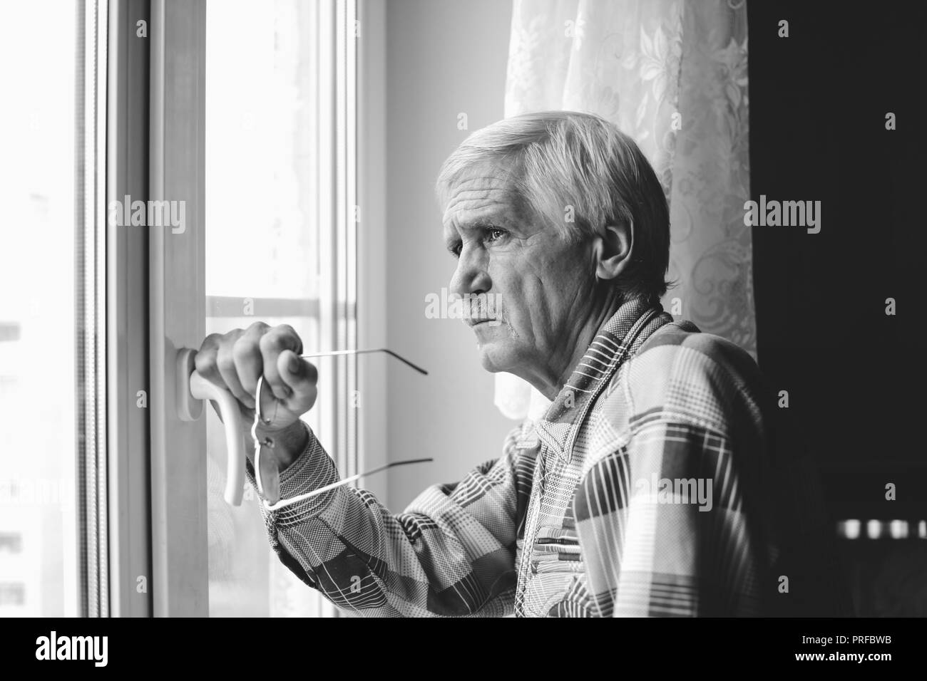 Porträt einer grauhaariger Mann 60 Jahre alt. Ein Mann schaut aus dem Fenster. Der Mann hat schlechtes Sehvermögen, er trägt eine Brille Stockfoto