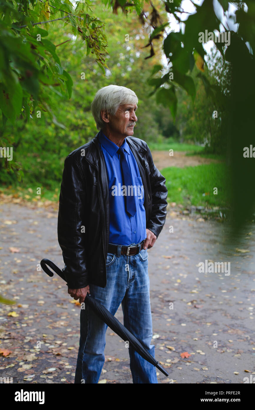 Grauhaariger Mann mit einem Regenschirm in der Hand auf der Straße. Ein Mann ist 60 Jahre alt. Stockfoto