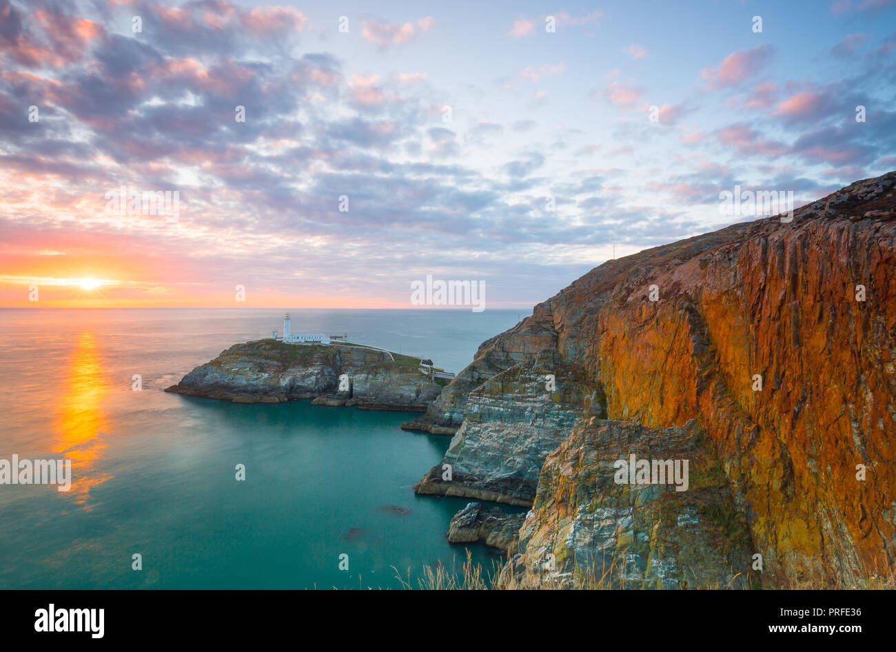 Abend Landschaft schoss der untergehenden Sonne mit Blick aufs Meer in Richtung South Stack Lighthouse, Anglesey, Nordwales. Glühende Felsen am späten Abend licht. Stockfoto