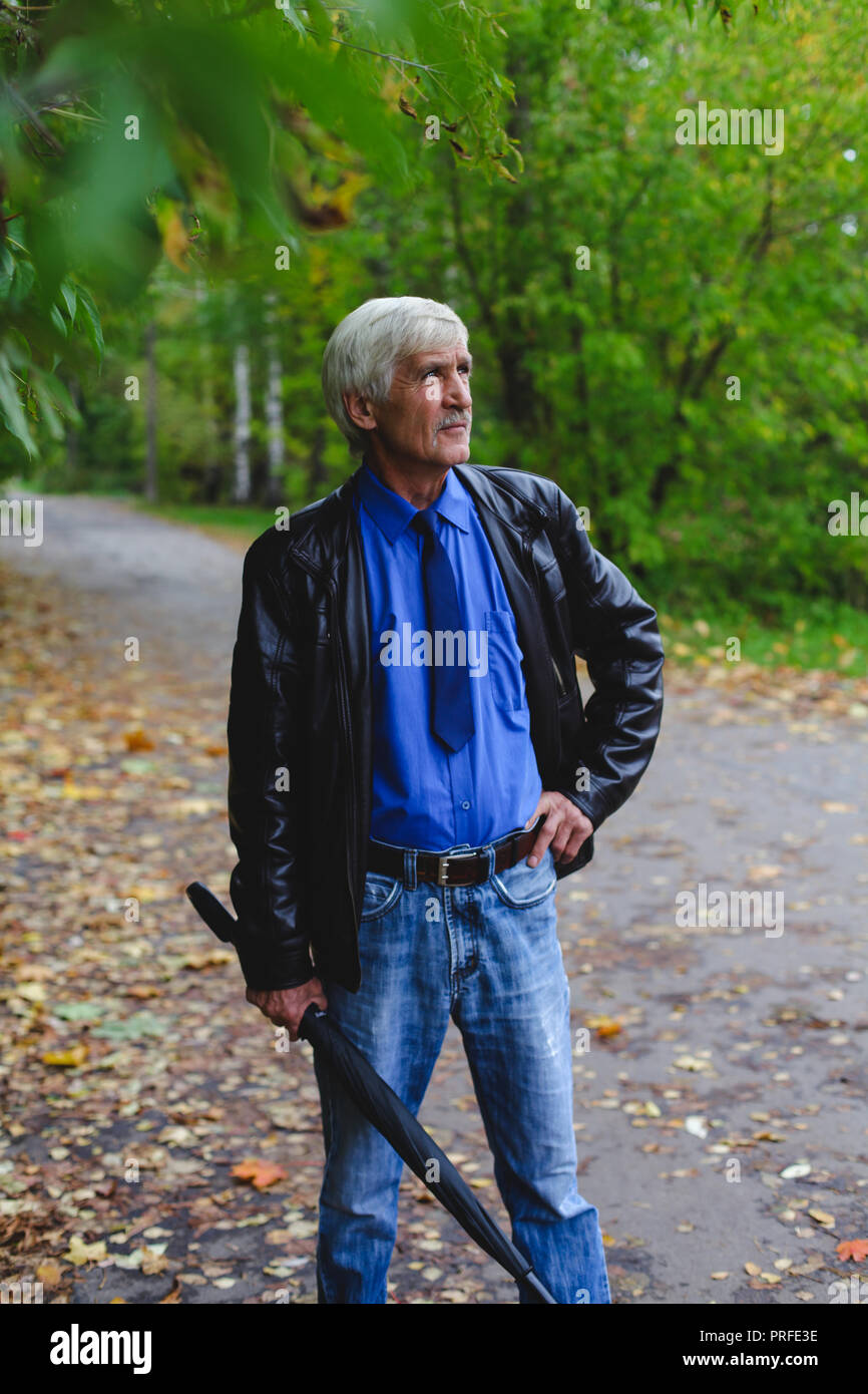 Grauhaariger Mann mit einem Regenschirm in der Hand auf der Straße. Ein Mann ist 60 Jahre alt. Stockfoto