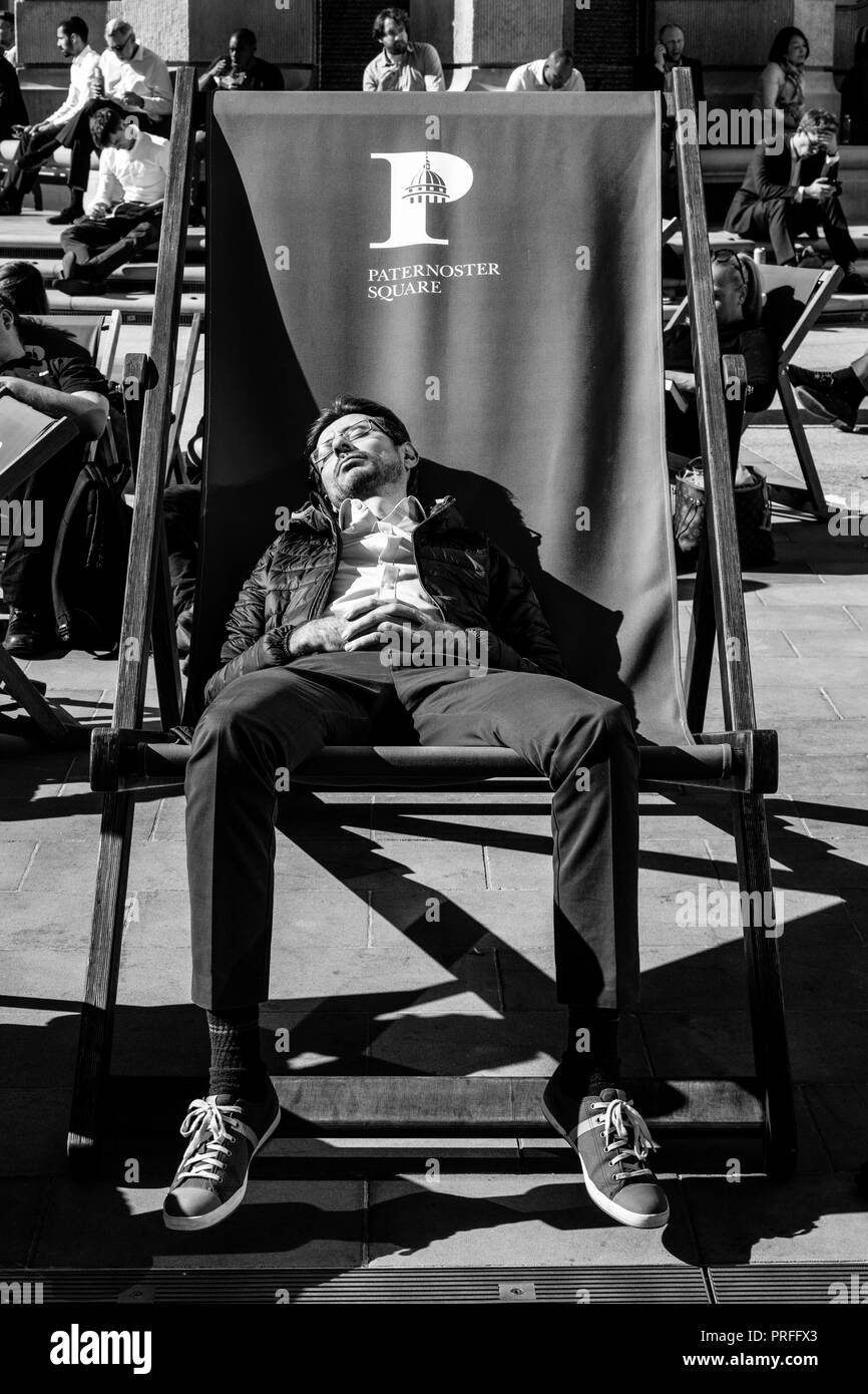 Ein junger Mann der schläft in einem übergrossen Liegestuhl während der Mittagspause, Paternoster Square, London, UK Stockfoto