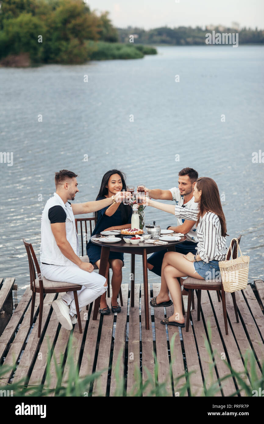 Prost! Eine Gruppe von Freunden ein Picknick im Freien Fluß Pier. Freundschaft, Essen und Spaß Konzept Stockfoto
