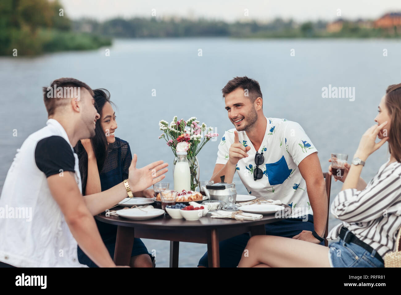 Gruppe der glückliche junge Freunde essen und Spaß im Außenbereich Restaurant am Fluss. Essen, Spaß und speisen Konzept Stockfoto