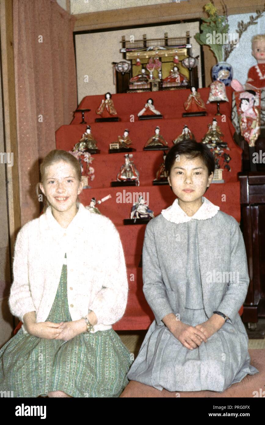 Zwei Mädchen vor einem ein wenig wie ein Altar mit japanischem Porzellan Figuren auf Regalen, 1965 gestapelt sitzen. () Stockfoto