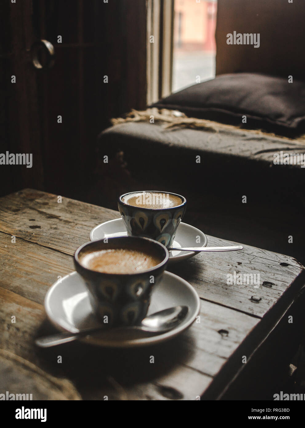 Zwei cortado Kaffees in handbemalten Tassen auf einen hölzernen Tisch in einem gemütlichen rustikalen Café Stockfoto