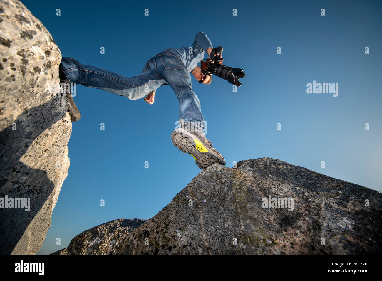 Mann Stepping über Geröll tragen Wanderschuhe und eine Kamera. Stockfoto