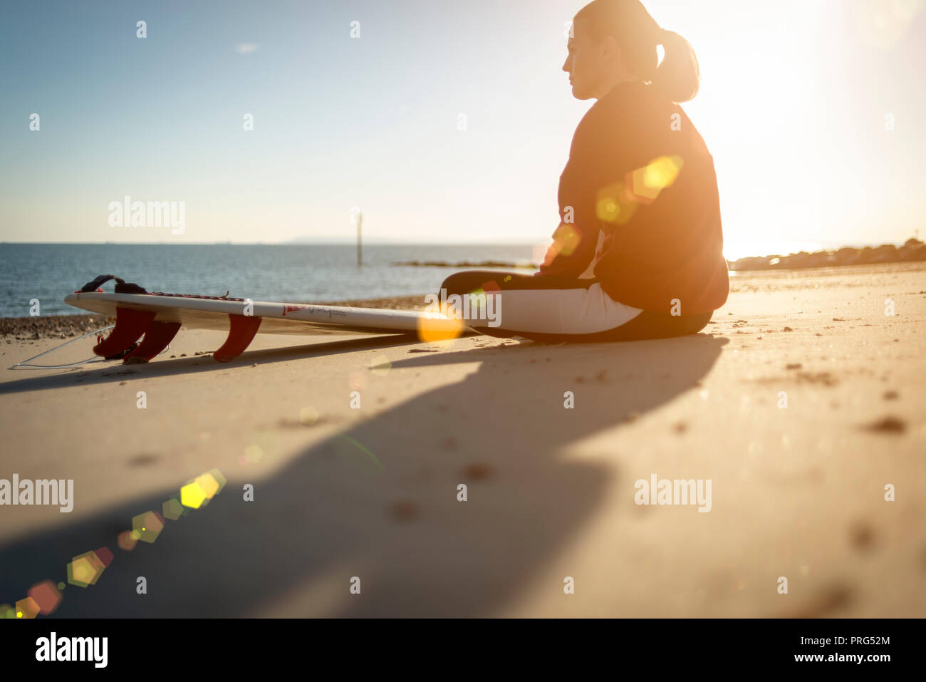 Frau Surfer am Strand zu sitzen mit ihrem Surfbrett beobachten die Wellen, lens flare Stockfoto