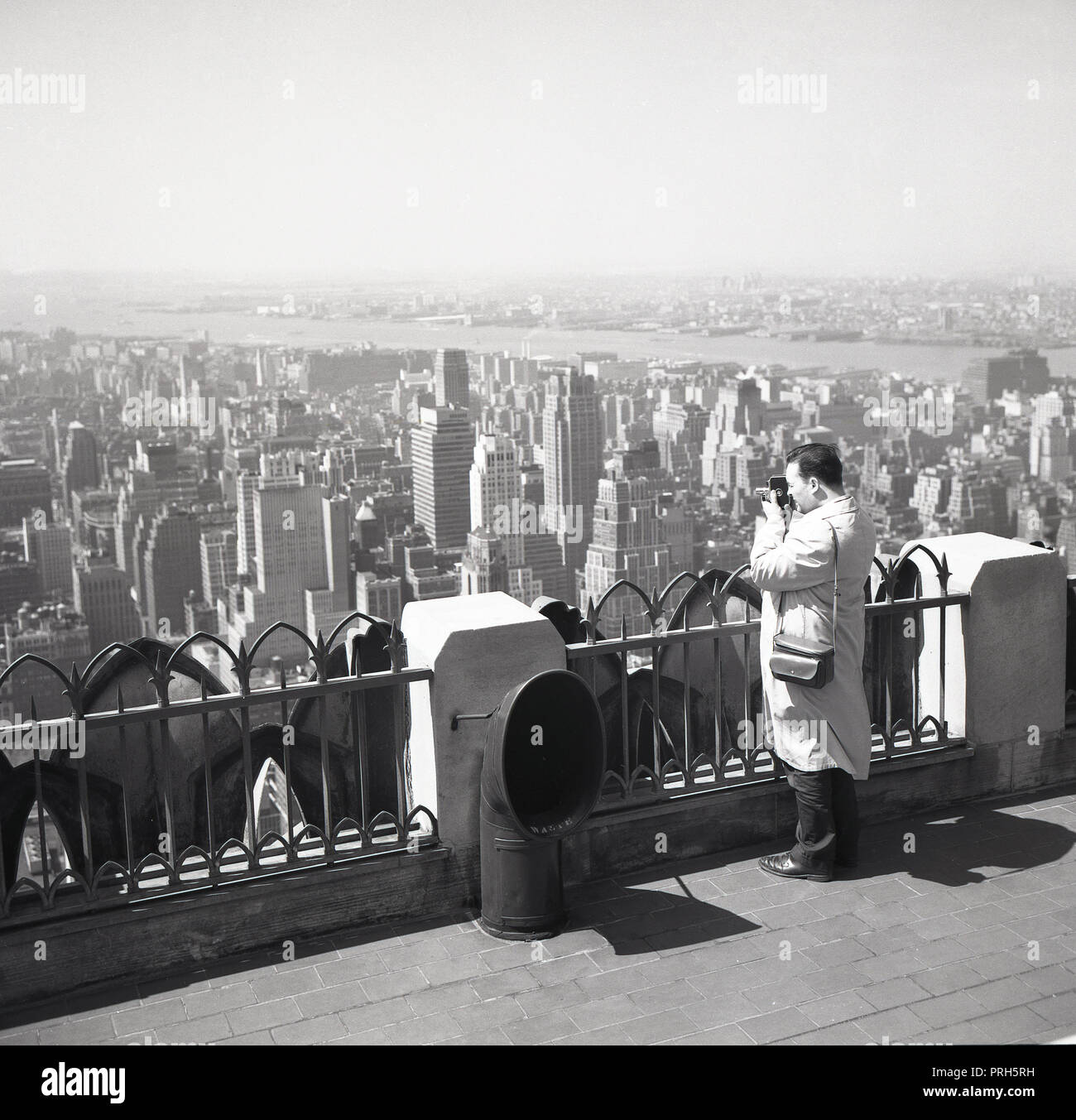 1950, historische, Mann mit einem cine Film Kamera und Blick auf die Skyline von New York City Film von der Spitze des Empire State Building, New York, NY, USA. Stockfoto