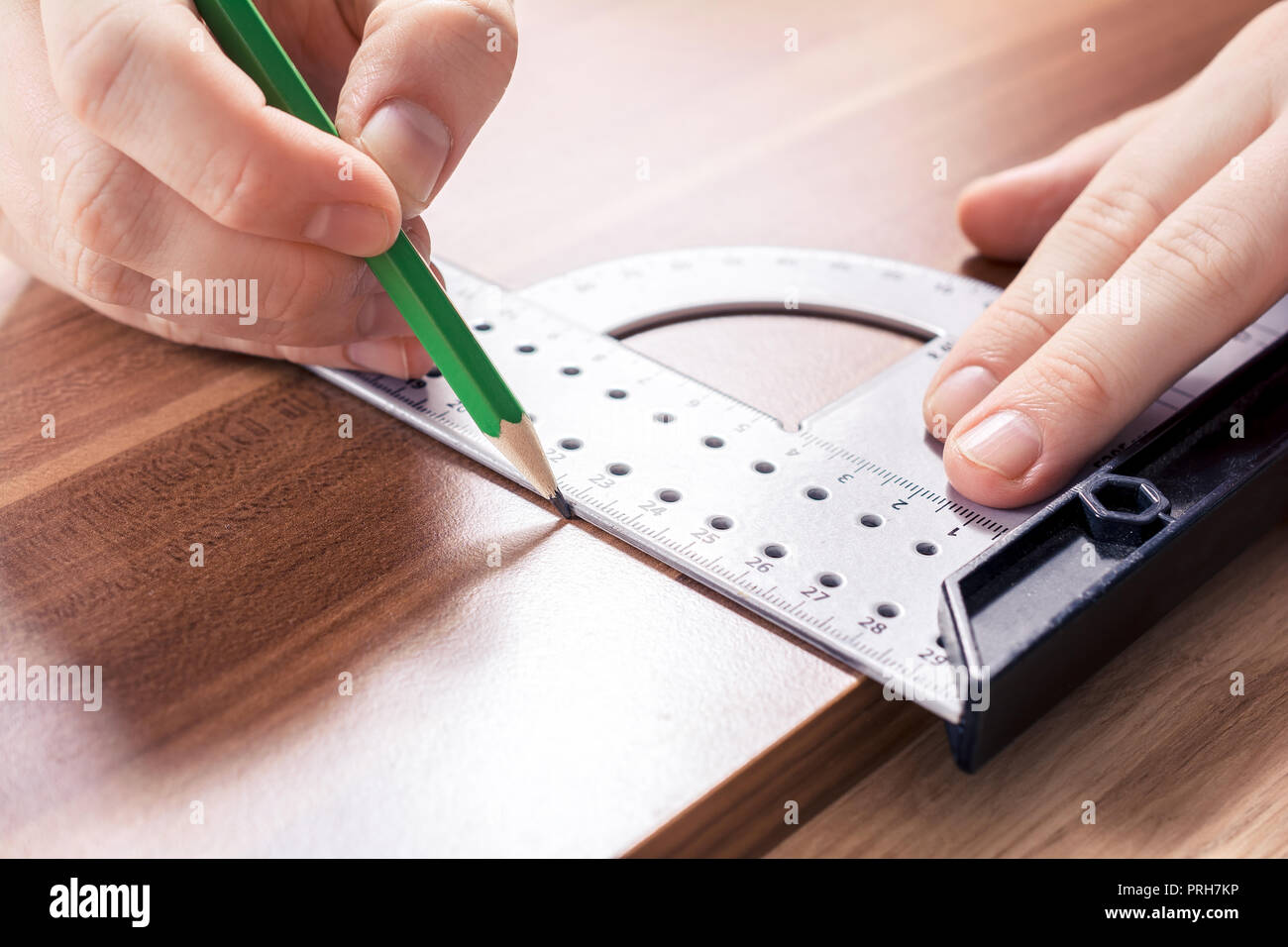 Hand mit einem Winkelmesser am Rande einer Holzplatte für einen rechten Winkel und dann machen Sie eine Markierung an der Messstelle mit einem Bleistift Stockfoto