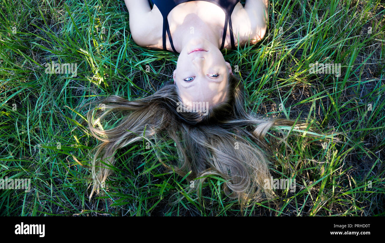 Portrait junge blonde Frau mit in das Gras mit langen Haaren und blauen Augen Stockfoto