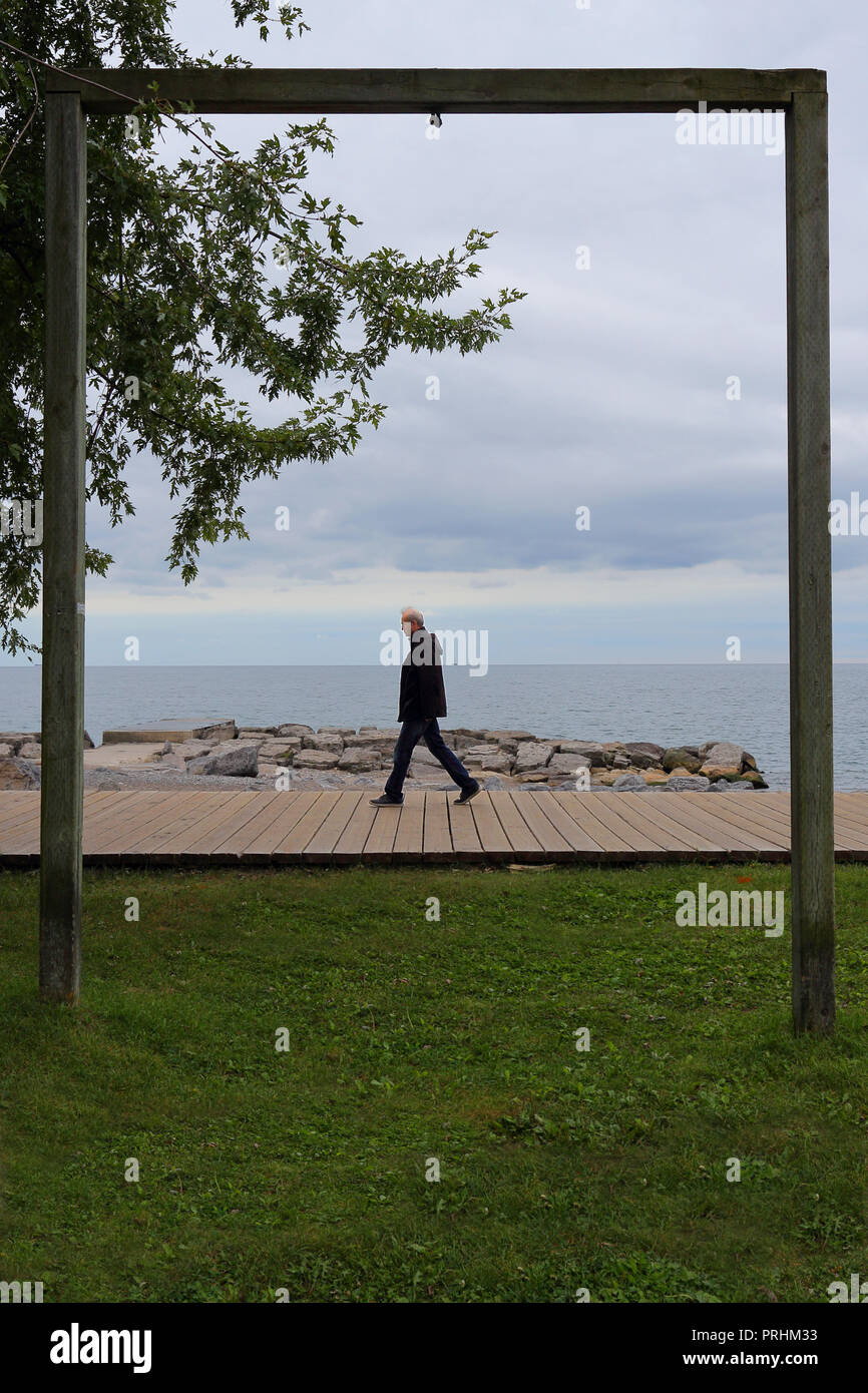 Geschossen von einem Mann zu Fuß auf eine Promenade, die von einem Rahmen aus Holz gerahmt. Ein See im Hintergrund gesehen werden. (Woodbine Strand, Toronto, CA) Stockfoto