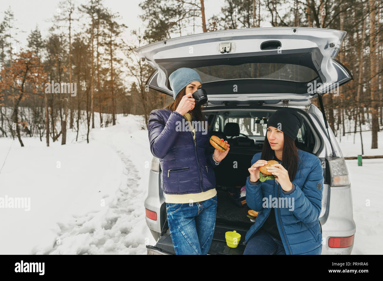 Freundinnen im Winter tragen auf verschneiten Tag im Winter Forest im Auto in Sprechen und trinken Kaffee Stockfoto