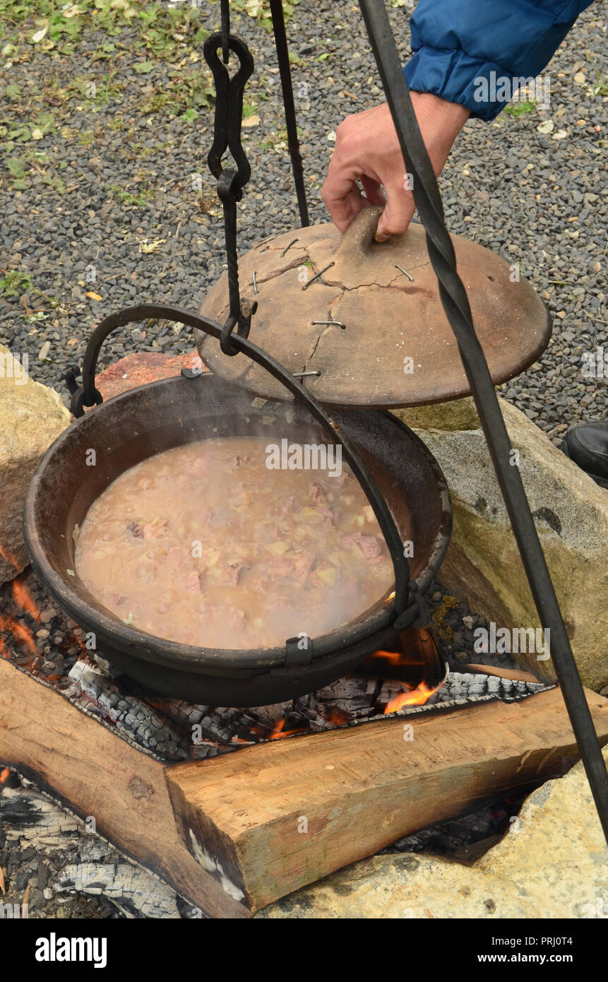 Vorbereiten der Gulasch auf offenem Feuer in einem Wasserkocher, Hebezeuge Ton Abdeckung, und prüfen Sie, ob ein Staat von Speise Stockfoto