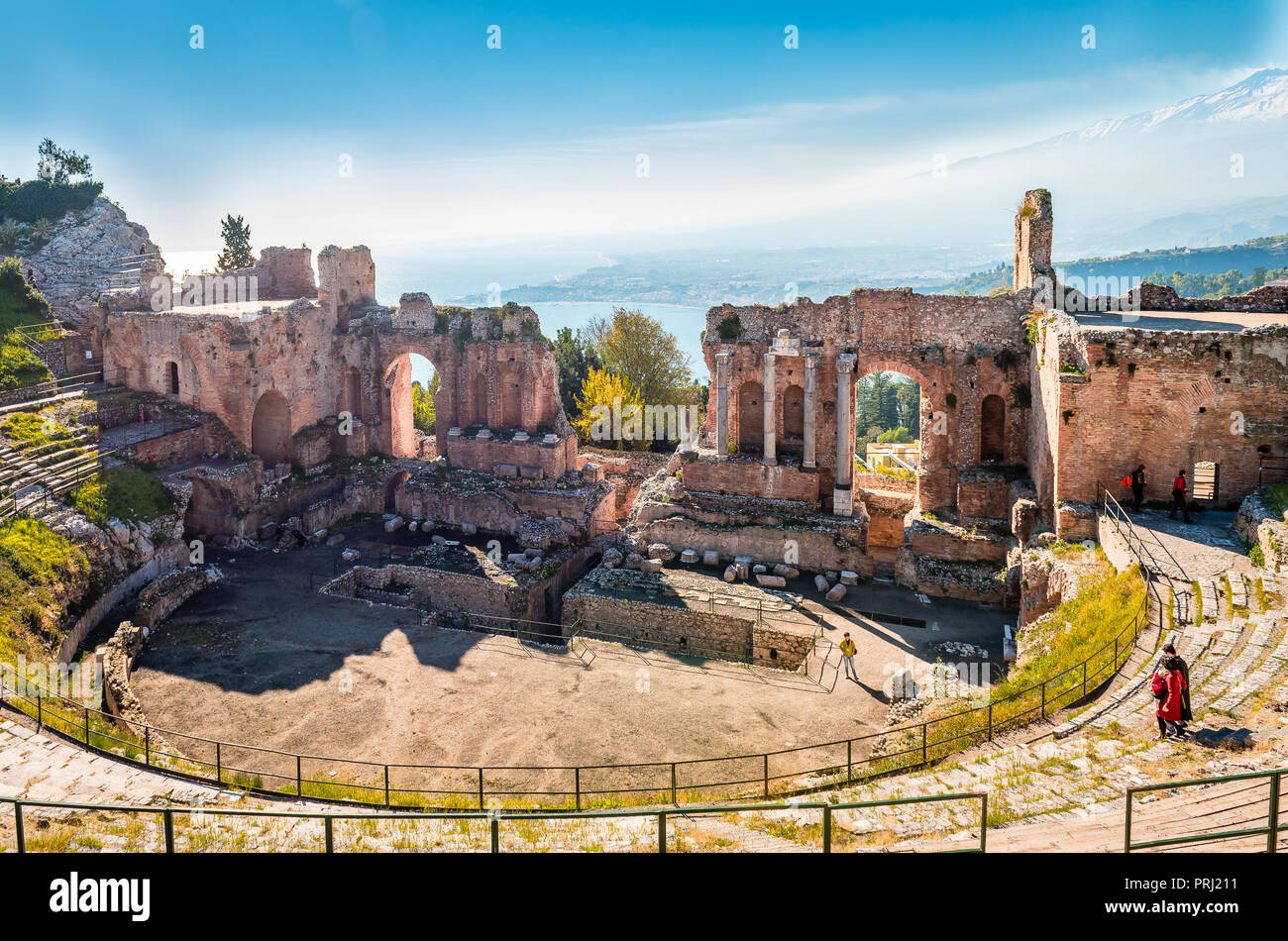 Taormina/Italien - 29. Dezember 2015: Blick auf das Teatro Greco (antike griechische Theater) mit dem Ionischen Meer und dem Rauchen schneebedeckten Ätna. Stockfoto