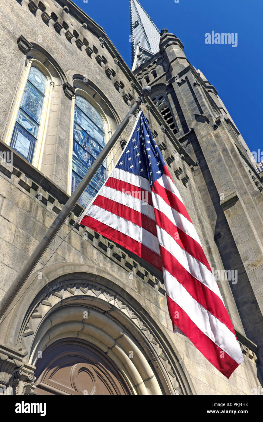 Eine US-Flagge hängt außerhalb der alten Steinkirche in Cleveland, Ohio und symbolisiert die Symbiose und die Trennung von Kirche und Staat. Stockfoto