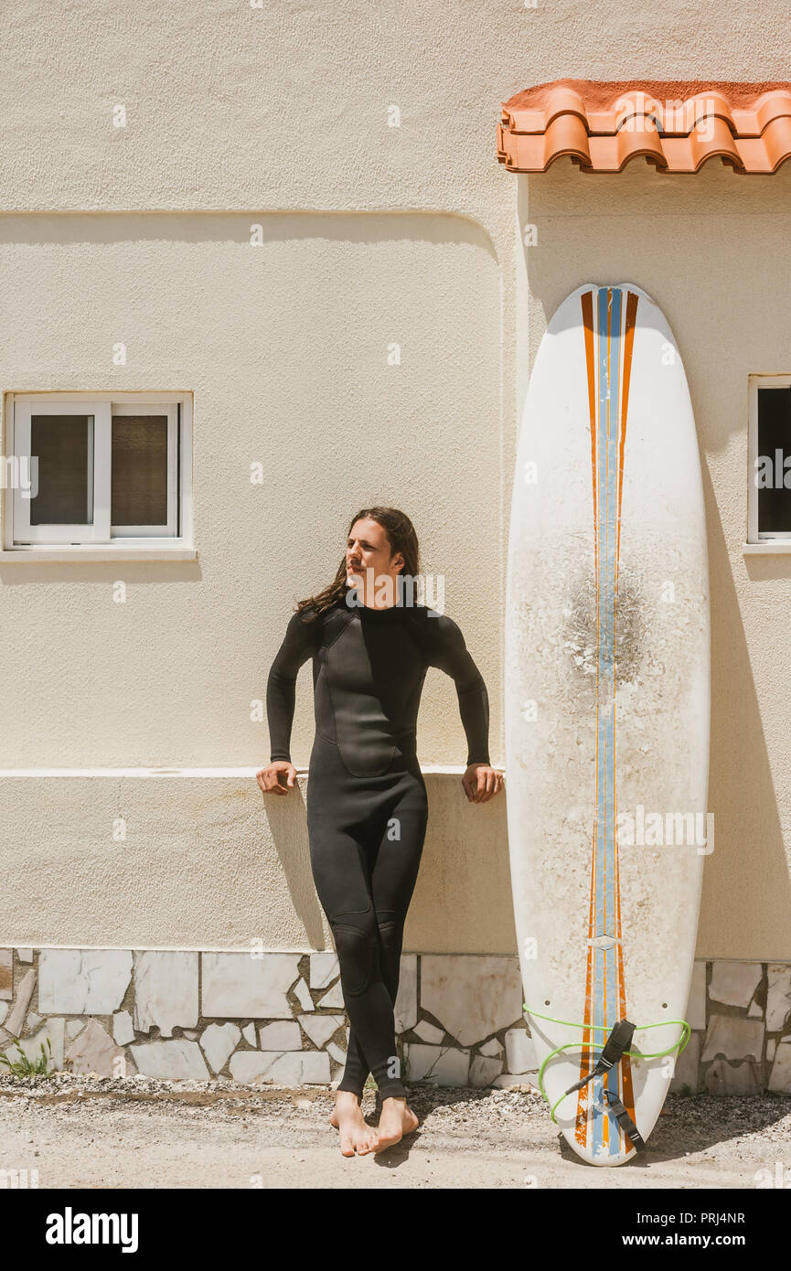 Junger Mann mit langen Haaren im Anzug auf der Straße in der Nähe Surfen in Portugal Stockfoto