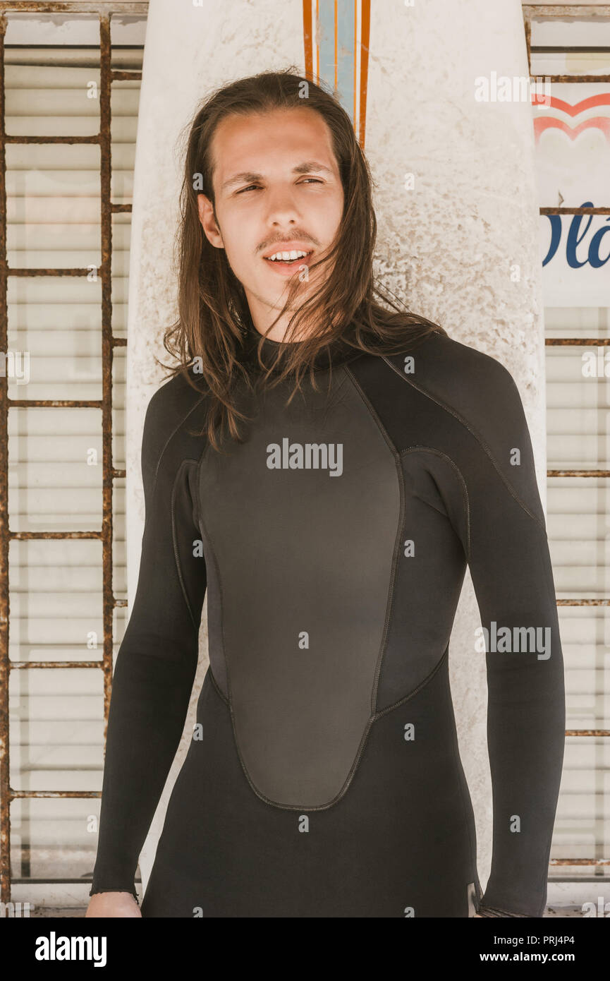 Porträt der Mann mit dem langen Haar in Neoprenanzug mit Surfen board weg schauen Stockfoto