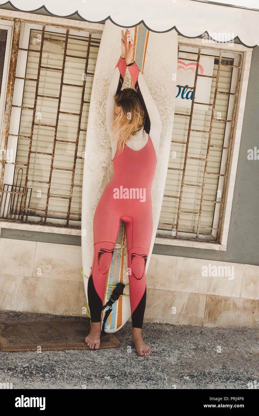 Junge Frau im Neoprenanzug mit Surfen board stehend gegen Gebäudewand in Portugal Stockfoto