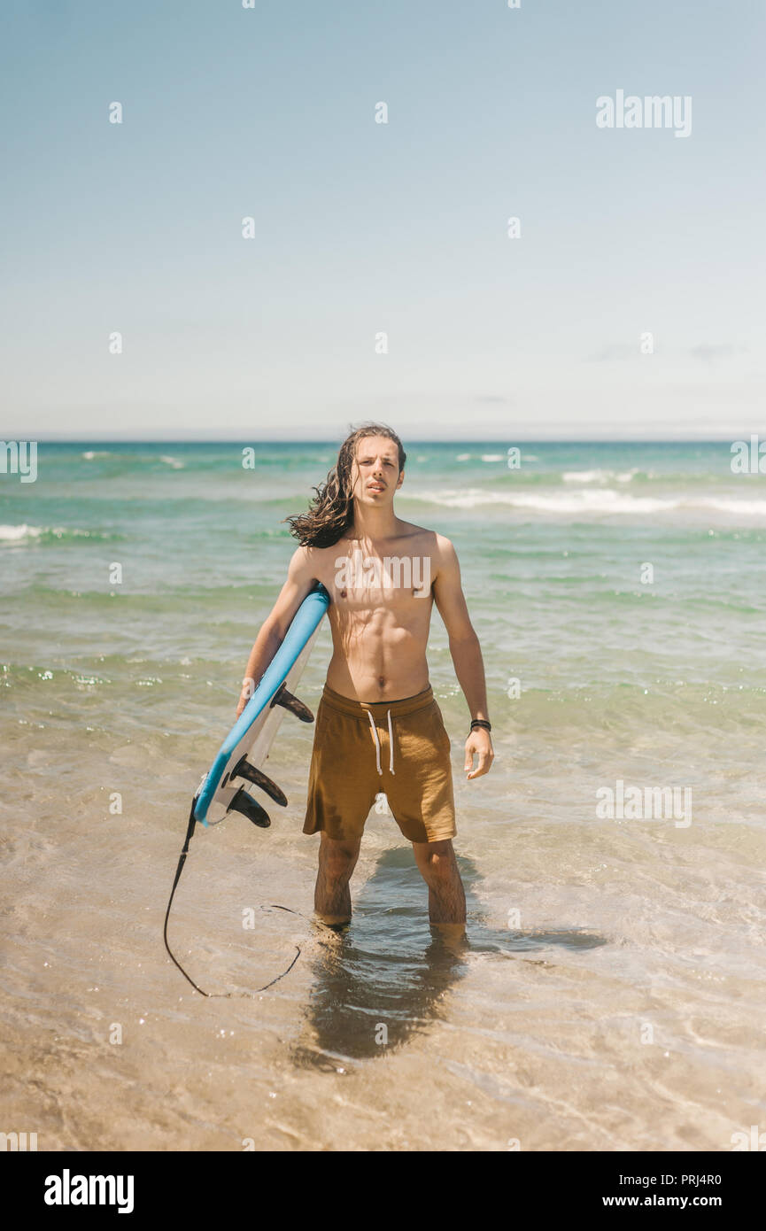 Junger Mann mit Surfbrett stehend im Ozean auf Sommer Tag Stockfoto