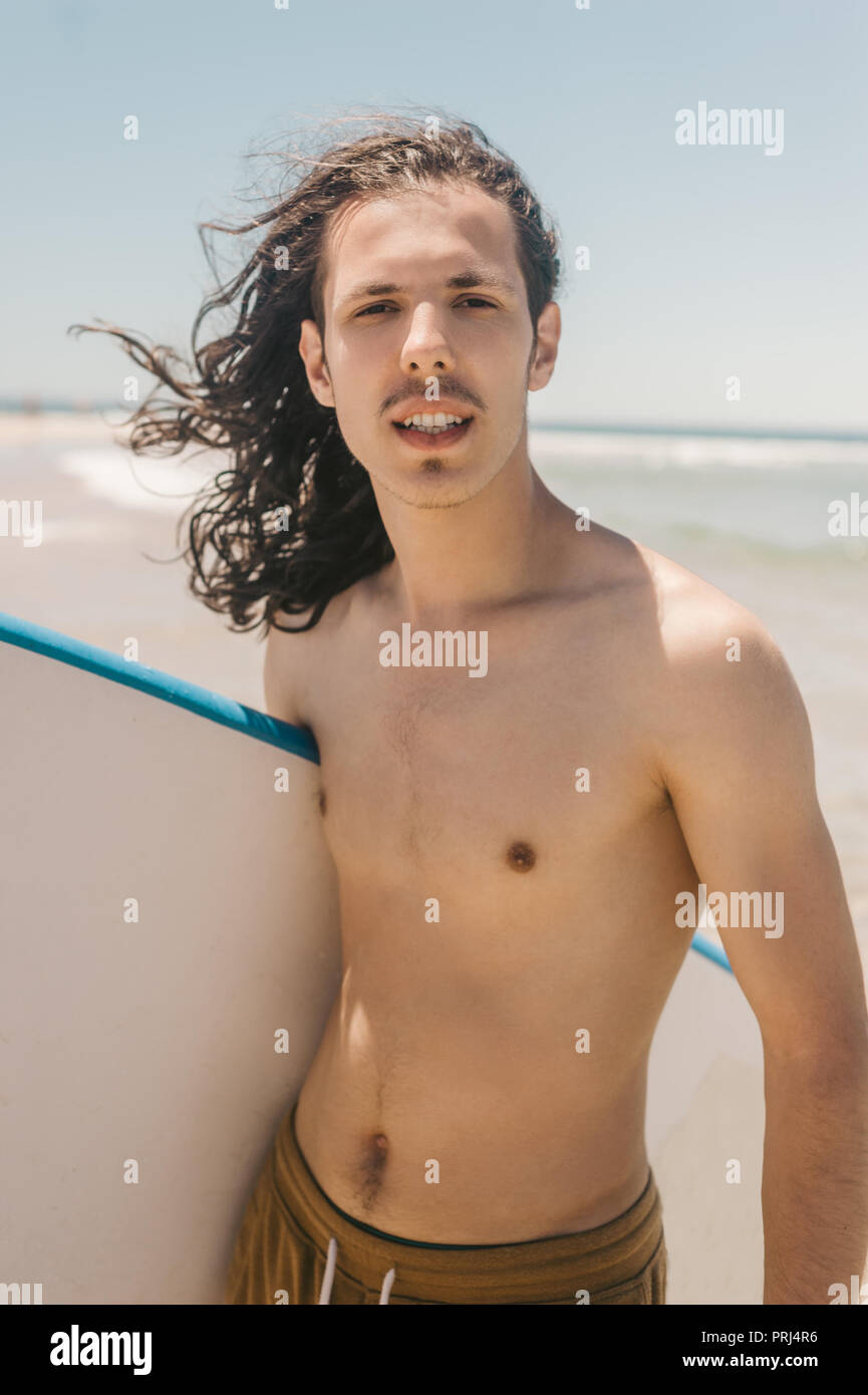 Porträt eines jungen Mannes mit Surfbrett mit Ozean auf Hintergrund auf Sommer Tag Stockfoto