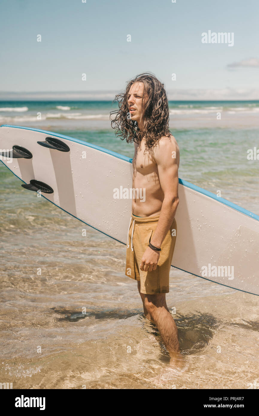 Junger Mann mit Surfbrett stehend im Ozean auf Sommer Tag Stockfoto