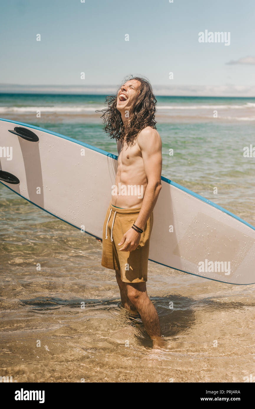 Junge glücklich Mann mit Surfbrett stehend im Ozean auf Sommer Tag Stockfoto