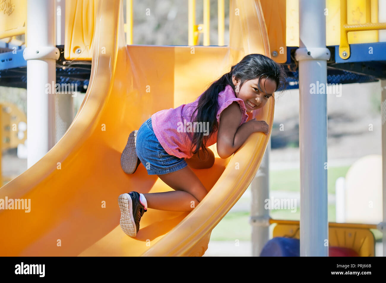 Junge Mädchen 5 Jahre alten Klettern auf einer Folie in einen Kinderspielplatz und genießen die körperliche Herausforderung Stockfoto
