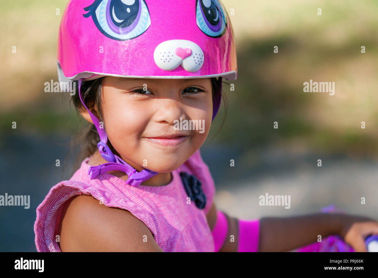 Lächelnde Mädchen mit niedlichen rosa Fahrrad Helm beim Lernen, ein Fahrrad im Sommer an einem Park zu fahren Stockfoto